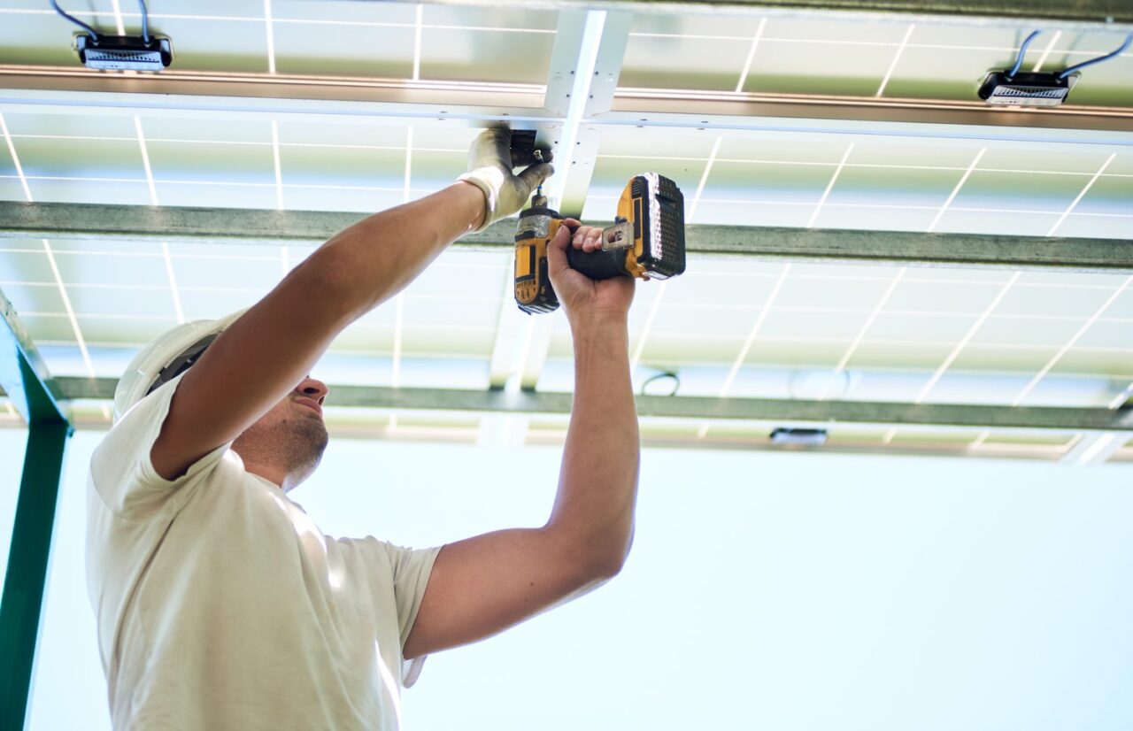 Un électricien inspecte les câbles et les spots d’une pergola après une coupure sous la pluie.