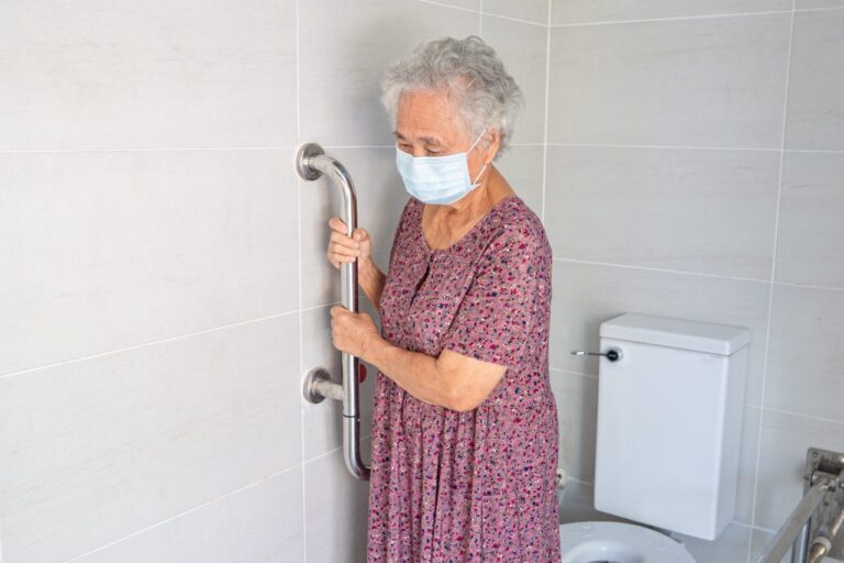 Un professionnel vérifie les installations électriques près d’une douche à l’italienne dans une salle de bain adaptée aux seniors.