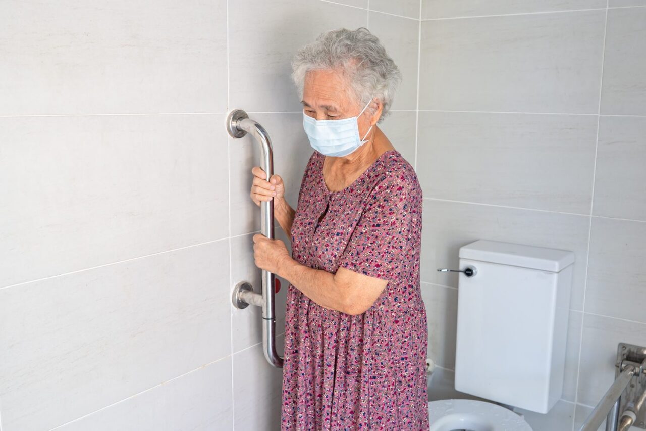 Un professionnel vérifie les installations électriques près d’une douche à l’italienne dans une salle de bain adaptée aux seniors.