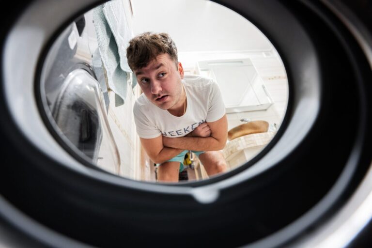 Une personne vidange un lave-linge rempli d’eau à l’aide d’un tuyau, avec une bassine posée au sol.